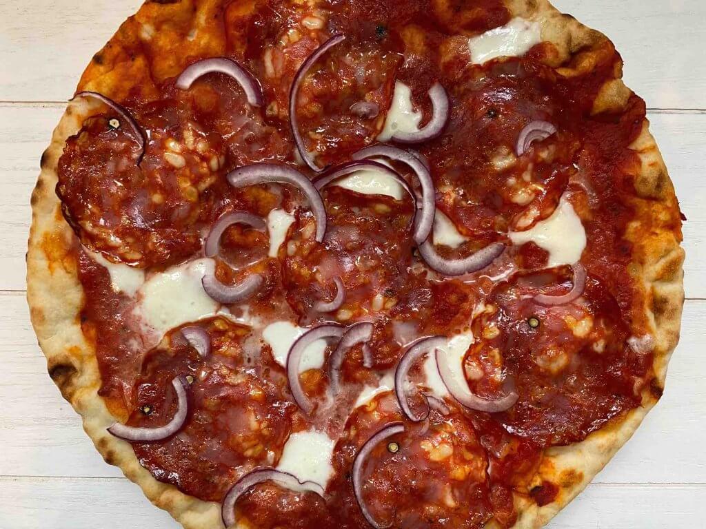 Pizza met pikante salami en rode ui